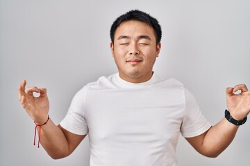 Young chinese man standing over white background relaxed and smiling with eyes closed doing meditation gesture with fingers. yoga concept.