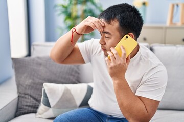 Young chinese man talking on the smartphone with worried expression at home