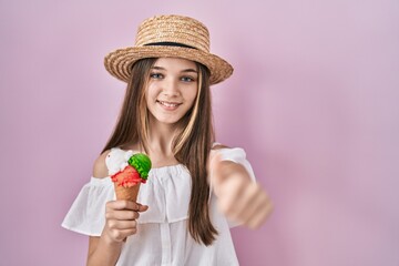 Teenager girl holding ice cream approving doing positive gesture with hand, thumbs up smiling and happy for success. winner gesture.