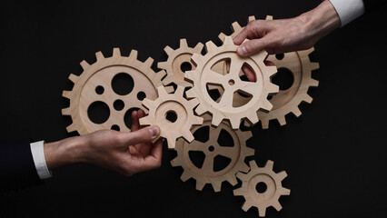 Group of business people connecting wooden cogwheels together. Office colleagues joining gears in...