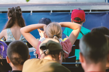 Children watch films sitting in a summer cinema.