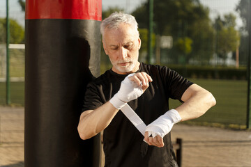 Pensioner senior man tying elastic bands on wrists, ready for boxing training
