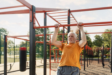Fototapeta premium Senior man, retired pensioner performs dips on bars on outdoor sports ground