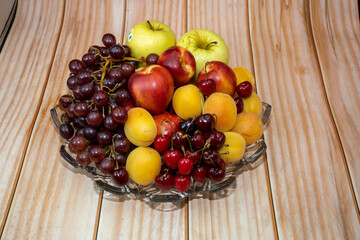 A plate of fruits consisting of grapes, peaches, apricots, cherries and apples on a wooden floor