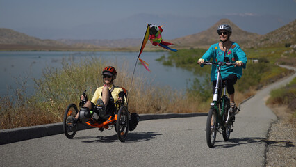 Mother and daughter biking up a hill next to a lake with mountains riding recumbent and normal...
