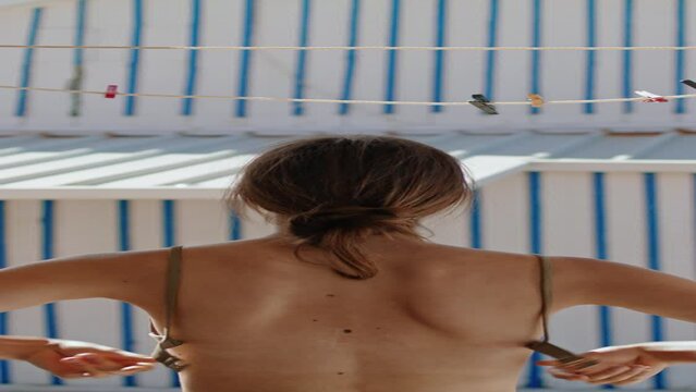 Topless girl taking bikini bra off in house vertically. Slim woman hang swimsuit