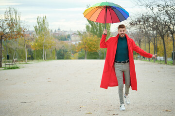 Latin young man with a red coat and rainbow umbrella walking on balance.