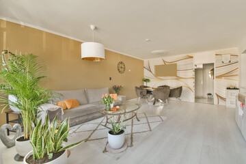a living room with couches and plants in the middle part of the room on the right is an open kitchen