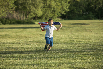 Fototapeta premium Kid boy celebrating of July, 4 Independence Day of USA . Child running with american flag symbol of United States over wheat field.