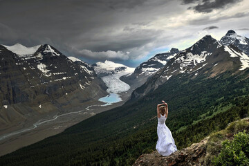 Woman white dress on cliff thunderstorm high wind storm glacier. Columbia ice field in Banff National park. Alberta. Canada
