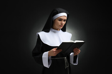 Young nun reading Bible on black background - obrazy, fototapety, plakaty
