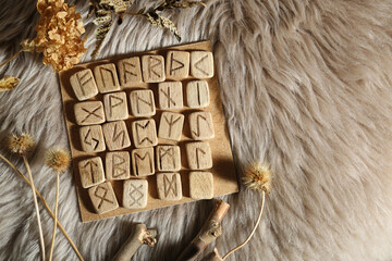 Many wooden runes and dried flowers on fur, flat lay. Space for text