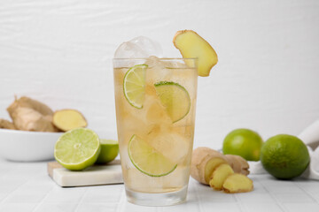 Glass of tasty ginger ale with ice cubes and ingredients on white tiled table