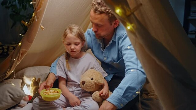 Happy dad spends time with daughter, snacking together inside a tent
