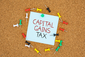 Capital gains tax text on light blue post-it paper pinned on bulletin cork board surrounding by...