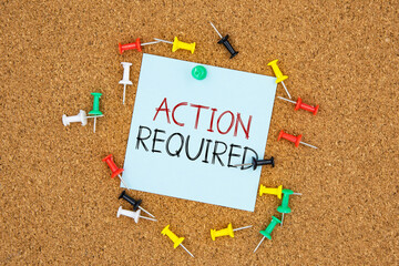 Action required text on light blue post-it paper pinned on bulletin cork board surrounding by multi color pins. This message can be used in business concept about taking action.