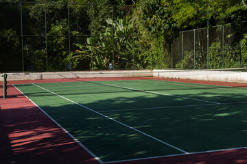 View of a green and red tennis court with nature all around. Widely used for sports and playing tennis