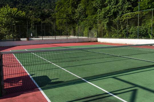 View of a green and red tennis court with nature all around. Widely used for sports and playing tennis