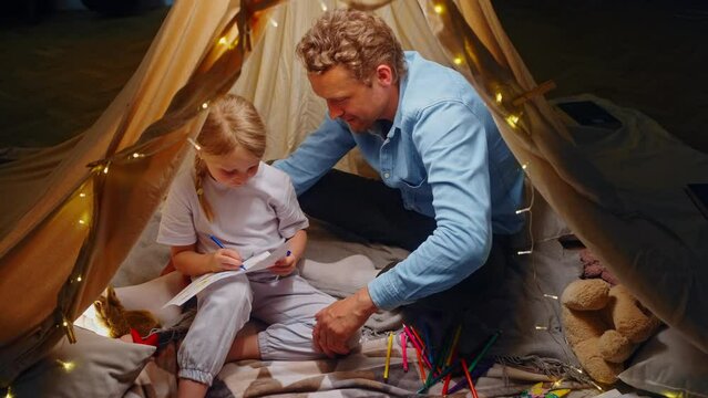 Beautiful little kid girl drawing pictures, enjoying wonderful moments with her dad inside a tent