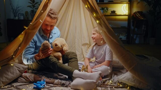 Cheerful dad and daughter play in theater of plush toys, enjoy happy time together inside game tent