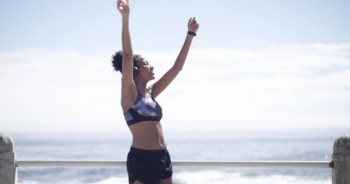 Music, headphones and fitness woman dance at a beach after training, running and morning cardio. Radio, dancing and female runner celebrating sports goal while listening to podcast after ocean run