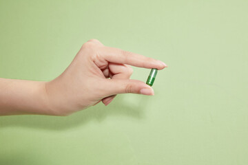 A female hand holding a single a green capsule of vitamin on a light green background. Drug concept...