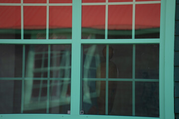 reflection in window of other windows with distortion from glass square window rectangular window panes antique green wooden window frame reflecting more green windows geometrical shapes backdrop 