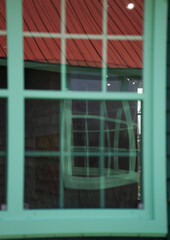 reflection in window of other windows with distortion from glass square window rectangular window panes antique green wooden window frame reflecting more green windows geometrical shapes backdrop 