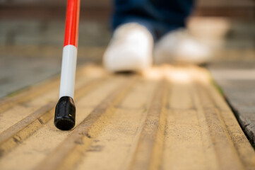 A blind woman walks on the street on tactile yellow tiles. Focus on the tactile cane. 