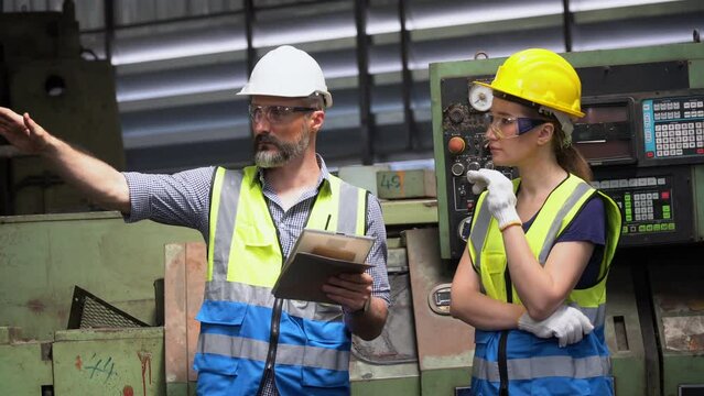 group of Two engineer man and technician worker repair machine discuss with tablet in steel metal manufacturing factory plant industry. team maintenance check quality machine. training explain work
