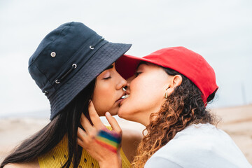 Lesbian couple with rainbow flag on hand kissing outdoors.