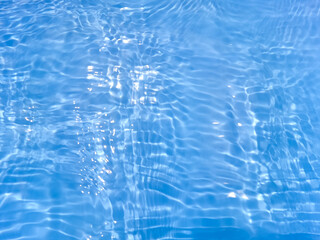 Blue water with ripples on the surface. Defocus blurred transparent blue colored clear calm water surface texture with splashes and bubbles. Water waves with shining pattern texture background.