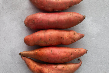 Raw sweet potatoes on a grey background. Orange kumara, yam. Healthy eating.