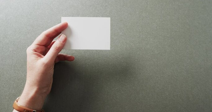 Hand of caucasian woman holding white business card on grey background, copy space, slow motion