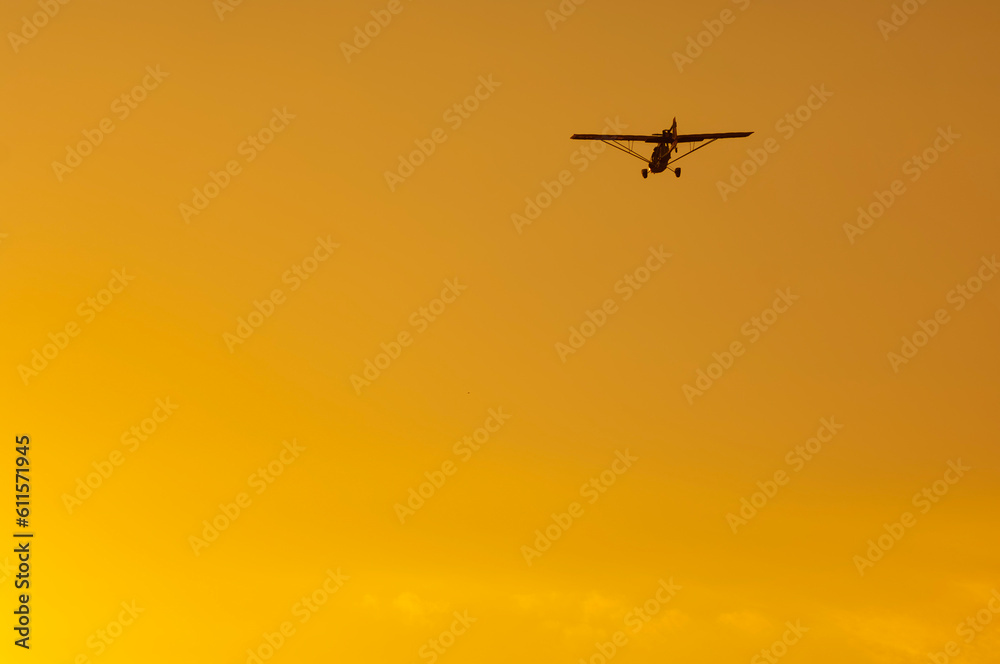 Wall mural ultralight plane silhouette in orange sky at sunset