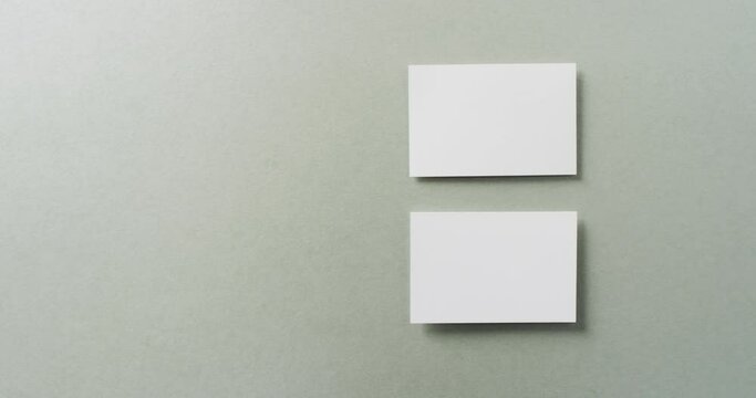 Overhead view of two white business cards arranged on grey background, copy space, slow motion