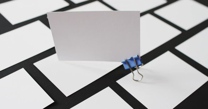 Blank white business card with bulldog clip standing on other blank cards, copy space, slow motion