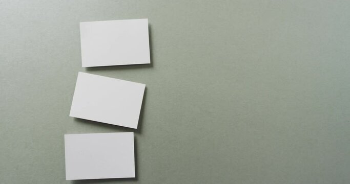 Overhead view of three white business cards arranged on grey background, copy space, slow motion