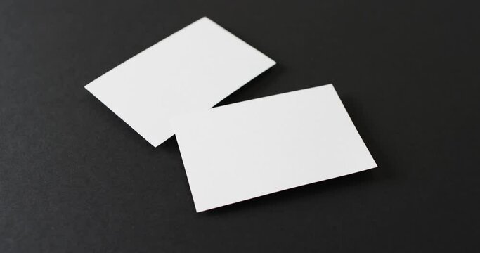 Close up of blank white business cards on black background, copy space, slow motion