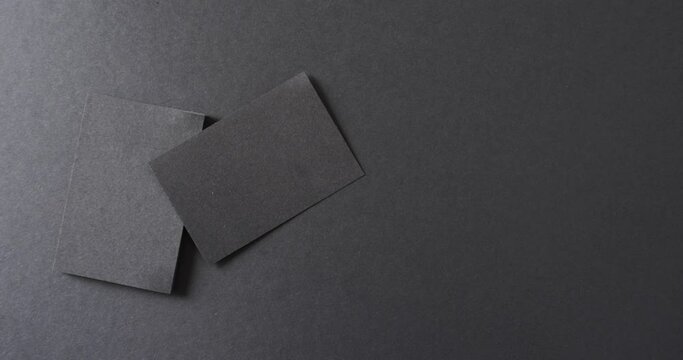 Overhead view of blank black business cards on black background, copy space, slow motion