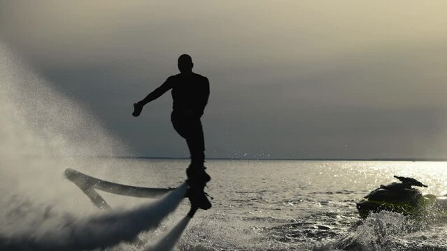 Water extreme. Flyboarder performs tricks over water. Silhouette of an unrecognizable male flyboarder