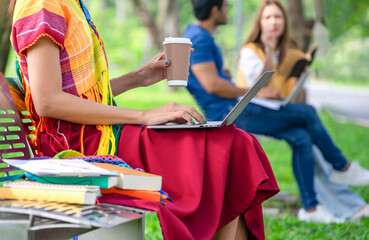 woman transgender in colorful rainbow lgbtq dresses one hand typing laptop,other hand holding a cup...