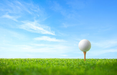 Golf ball with tee on green grass with blue sky background.