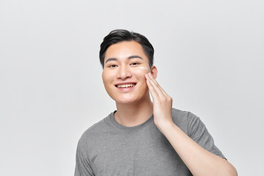 Close up beauty portrait of half naked satisfied young man applying facial cream
