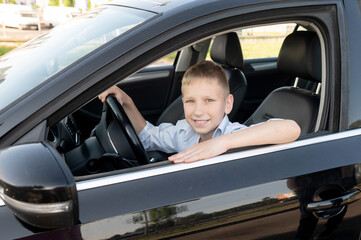 A cute boy is sitting behind the wheel of a car and smiling