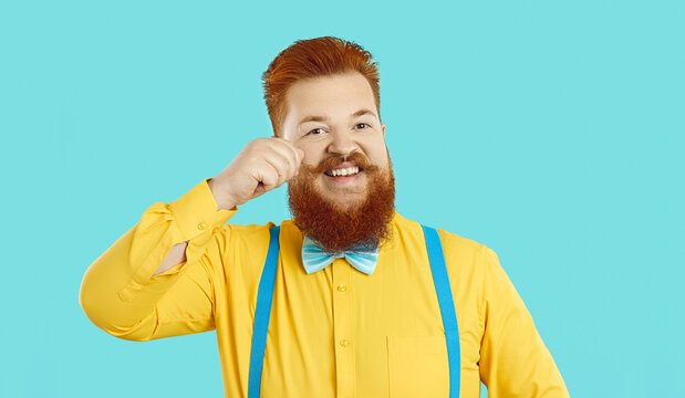 Headshot portrait of funny bearded redhead man isolated on blue studio background in suit with bow. Profile picture of smiling young red-haired man with mustache feel optimistic and overjoyed.