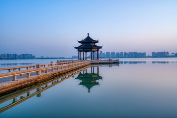 A pavilion and its reflection in the lake. Modern skyscrapers in distance. Photo is taken in...
