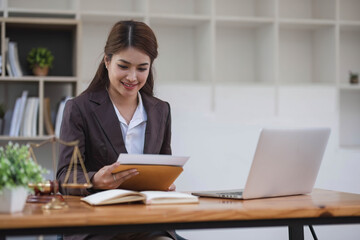 Looking camera. Young Attractive Asian female lawyer working in office with contract and law books when sitting at desk. Law, legal services, advice, Justice and real estate concept.