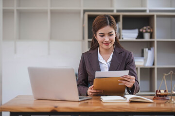 Looking camera. Young Attractive Asian female lawyer working in office with contract and law books when sitting at desk. Law, legal services, advice, Justice and real estate concept.