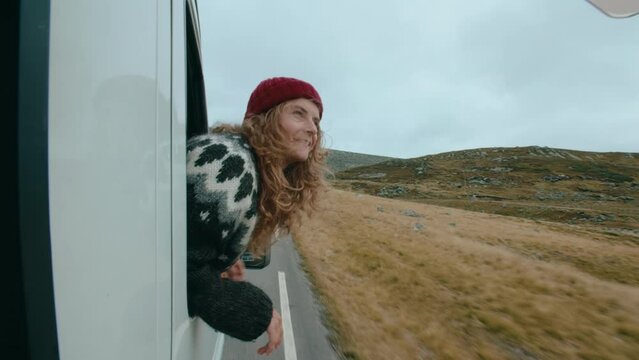Handheld shot of young woman lean out of car window during amazing road trip around Norway. Look around at scenery. Wanderlust cinematic adventure trip for young people, camping in RV